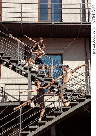 The group of modern ballet dancers performing on the stairs at the city 67647574
