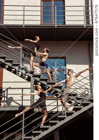 The group of modern ballet dancers performing on the stairs at the city 67647576