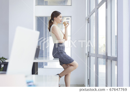Beautiful female office worker sits at the desk and spends coffee time Beautiful female office worker sits at the desk and spends coffee time 67647769