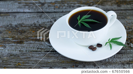 Cup of cannabis coffee with hemp leaves and roasted coffee beans on wooden table Cup of cannabis coffee with hemp leaves and roasted coffee beans on wooden table 67650566