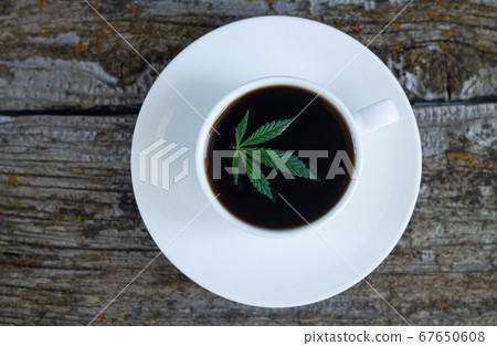 Cannabis coffee - marijuana leaf on coffee cup, rustic wooden background Cannabis coffee - marijuana leaf on coffee cup, rustic wooden background 67650608