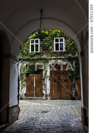Courtyard Of A HIstoric Building With Wooden Doors And Ivy Overgrown Walls 67651304