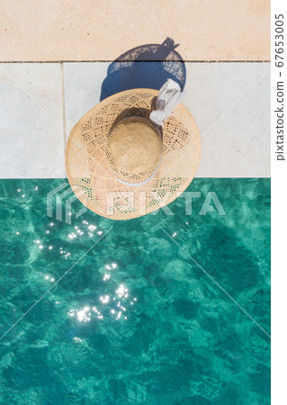 Woman wearing big summer sun hat relaxing on pier by clear turquoise sea. 67653005