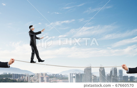 Business concept of risk support and assistance with man balancing on rope Business concept of risk support and assistance with man balancing on rope 67660570
