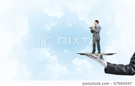 Businessman on metal tray playing fife against blue sky background Businessman on metal tray playing fife against blue sky background 67660947