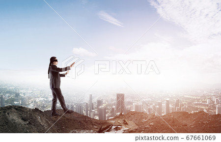 Young businessman in blindfold walking carefully and cityscape at background 67661069