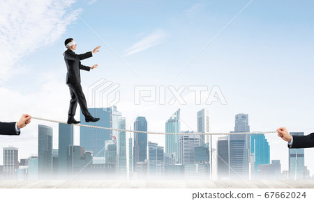 Business concept of risk support and assistance with man balancing on rope Business concept of risk support and assistance with man balancing on rope 67662024