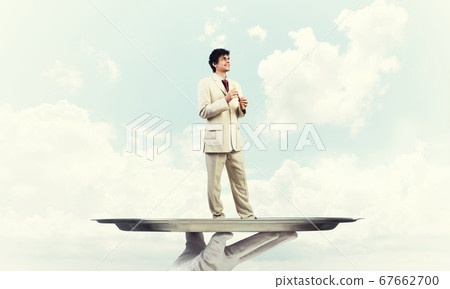 Businessman on metal tray playing fife against blue sky background Businessman on metal tray playing fife against blue sky background 67662700