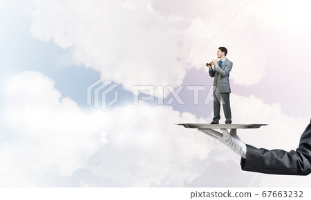 Businessman on metal tray playing fife against blue sky background 67663232
