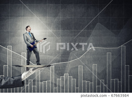 Businessman on metal tray playing electric guitar against graphs background Businessman on metal tray playing electric guitar against graphs background 67663984