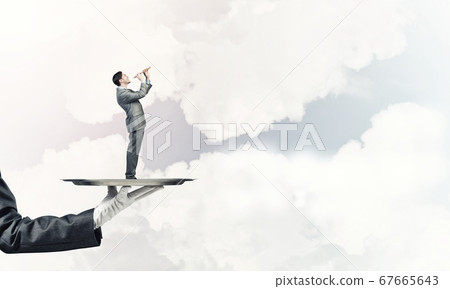Businessman on metal tray playing fife against blue sky background 67665643