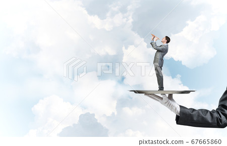 Businessman on metal tray playing fife against blue sky background Businessman on metal tray playing fife against blue sky background 67665860