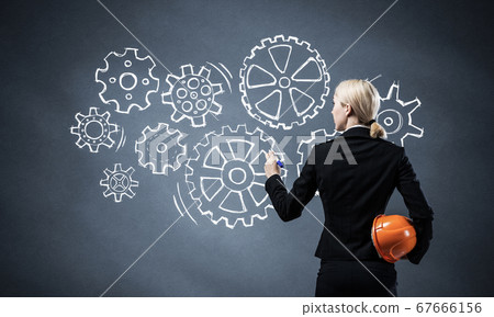 Businesswoman draws gears mechanism on blackboard Businesswoman draws gears mechanism on blackboard 67666156