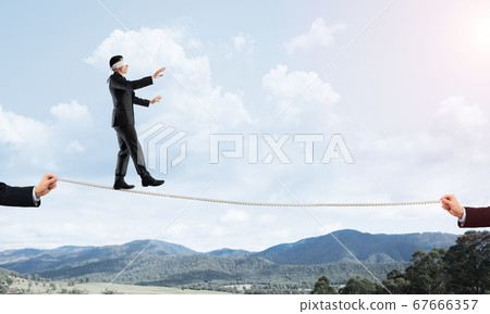 Business concept of risk support and assistance with man balancing on rope Business concept of risk support and assistance with man balancing on rope 67666357