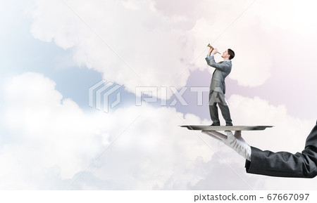 Businessman on metal tray playing fife against blue sky background Businessman on metal tray playing fife against blue sky background 67667097