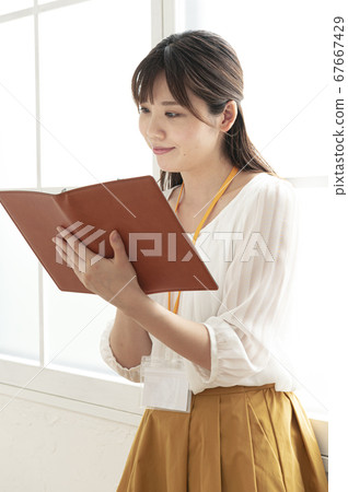Young woman looking at a leather notebook by the window Young woman looking at a leather notebook by the window 67667429