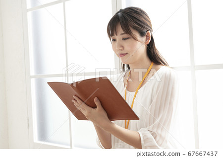 Young woman looking at a leather notebook by the window Young woman looking at a leather notebook by the window 67667437