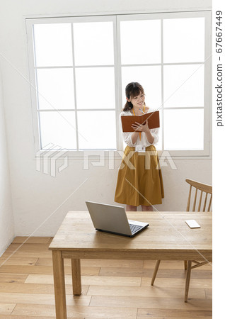 Young woman looking at a leather notebook by the window Young woman looking at a leather notebook by the window 67667449