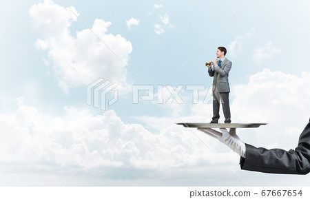Businessman on metal tray playing fife against blue sky background Businessman on metal tray playing fife against blue sky background 67667654