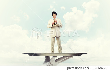 Businessman on metal tray playing fife against blue sky background Businessman on metal tray playing fife against blue sky background 67668226