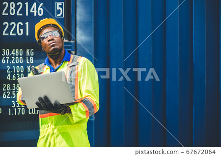 Black African worker working in logistic shipping using laptop to control loading containers 67672064
