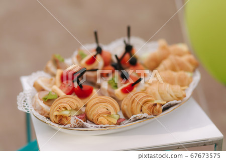Croissant sandwich with ham and tartalets with red fish and olive on plate outdoors. Party on terrace Croissant sandwich with ham and tartalets with red fish and olive on plate outdoors. Party on terrace 67673575