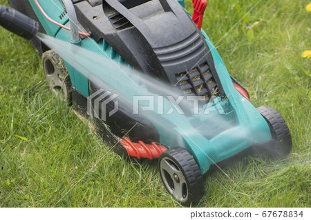 jet of water from high-pressure washer cleans dirty lawn mower on green grass jet of water from high-pressure washer cleans dirty lawn mower on green grass 67678834