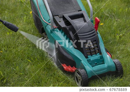 jet of water from high-pressure washer cleans lawn mower on green grass 67678889