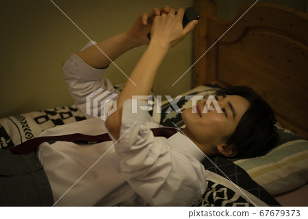 Student watching smartphone in bed 67679373