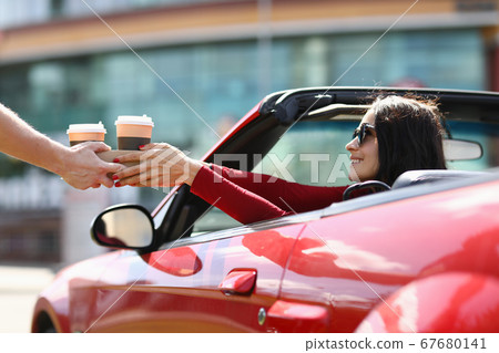 Woman in cabriolet picks up hot drinks from a courier 67680141
