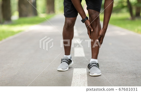 Black sportsman touching his aching leg while jogging outdoors 67681031