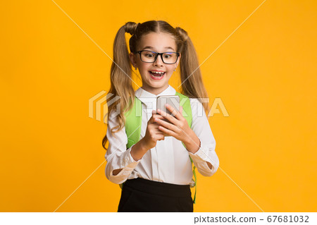 Excited Elementary Student Girl Using Smartphone Doing Homework, Studio Shot Excited Elementary Student Girl Using Smartphone Doing Homework, Studio Shot 67681032