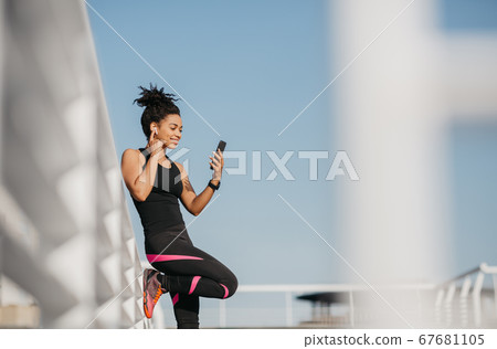 Music for run. African american girl in sportswear puts wireless headphones and watches at smartphone Music for run. African american girl in sportswear puts wireless headphones and watches at smartphone 67681105