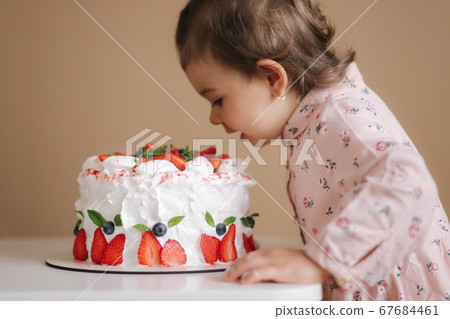 Little girl first time taste bithday cake. Cute little girl in beautiful dress tasting cake with strawberries Little girl first time taste bithday cake. Cute little girl in beautiful dress tasting cake with strawberries 67684461