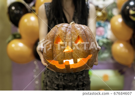 Young adult woman hold in hand spooky custom weird handmade orange pumpkin head with carved faces and glowing candle or light inside. Halloween party decoration celebrate traditional autumn holiday 67684607