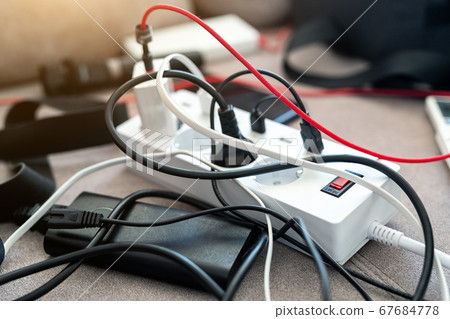 Overloaded power socket plug extendion at home. Tangled cords of home appliances and chargins gadgets mess Overloaded power socket plug extendion at home. Tangled cords of home appliances and chargins gadgets mess 67684778