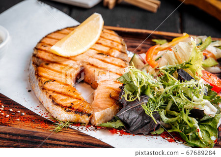 Grilled salmon steak with greens salad and lemon 67689284