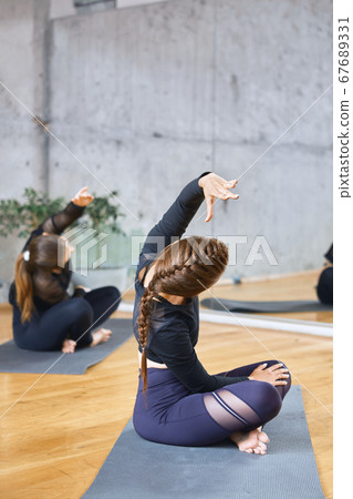 Women practicing practicing lotus pose in hall. 67689331