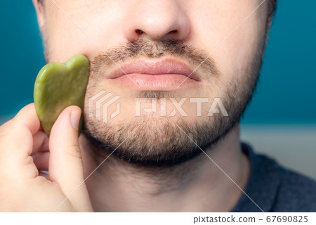 Bearded man is using jade face roller 67690825