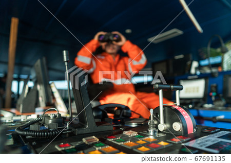 Filipino deck Officer on bridge of vessel or ship looking through binoculars 67691135