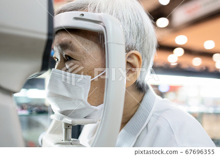 Asian senior woman having eyesight test using tonometer looking into the machine,old elderly patient checks her vision,eye examination by ophthalmlogist,presbyopia problems,health care at eye clinic 67696355