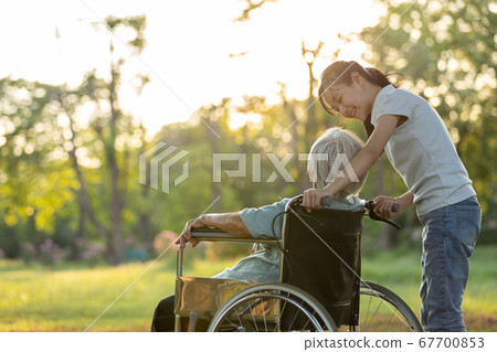 Happy old senior woman in wheelchair with granddaughter walking outdoor at park,smiling child girl and elderly grandmother rest and talking together evening in sunset nature,love,family relationships 67700853