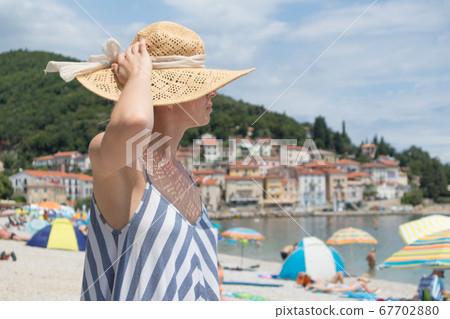 Lady wearing striped summer dress and straw hat relaxing on vaction enjoying view over beach at Moscenicka Draga, Istria, Croatia 67702880