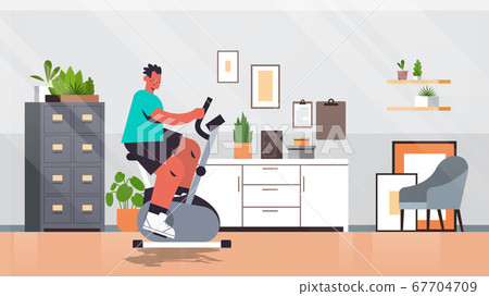 man riding stationary bike at home guy having workout cardio fitness training healthy lifestyle sport 67704709