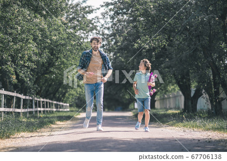 Dark-haired boy with a skateboard and his father running in the park Dark-haired boy with a skateboard and his father running in the park 67706138