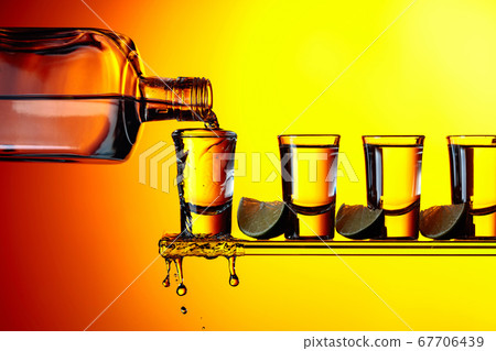 Tequila with lime slices on a yellow background. Tequila with lime slices on a yellow background. 67706439