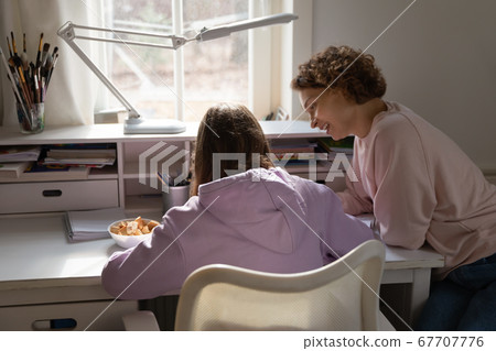 Smiling mother helping to teenage daughter with school assignment Smiling mother helping to teenage daughter with school assignment 67707776