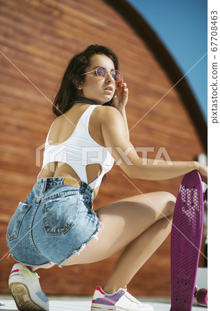 Beautiful brunette girl in shorts sitting near the skateboard 67708463