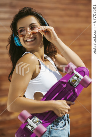 Beautiful brunette girl holding a skateboard and smiling Beautiful brunette girl holding a skateboard and smiling 67708501