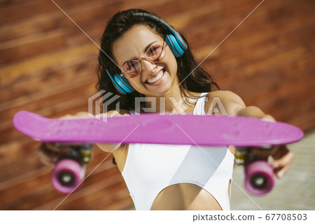 Beautiful brunette girl showing a skateboard and smiling Beautiful brunette girl showing a skateboard and smiling 67708503